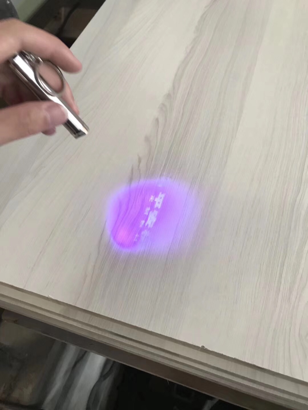 手持幼型灯具照向板面，紫色光斑内可见淡色字符
