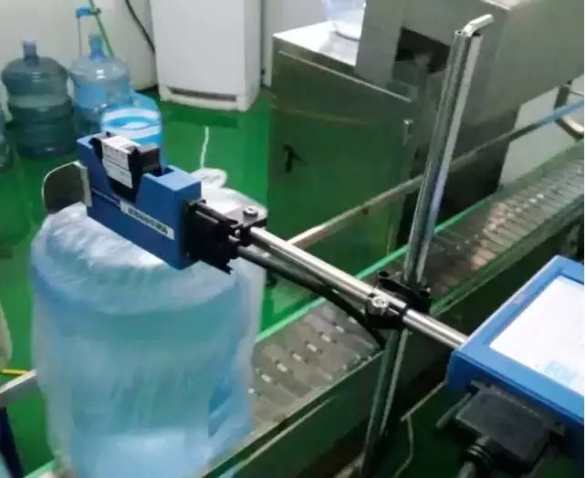 输送链上的大号水桶与桶口旁蓝色设备及支架