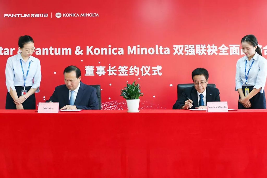 奔图与KONICA MINOLTA标识布景前两人坐桌具名