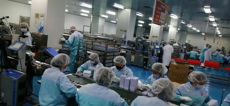 戴口罩帽子和手套的人员围在包装设备及传送带旁