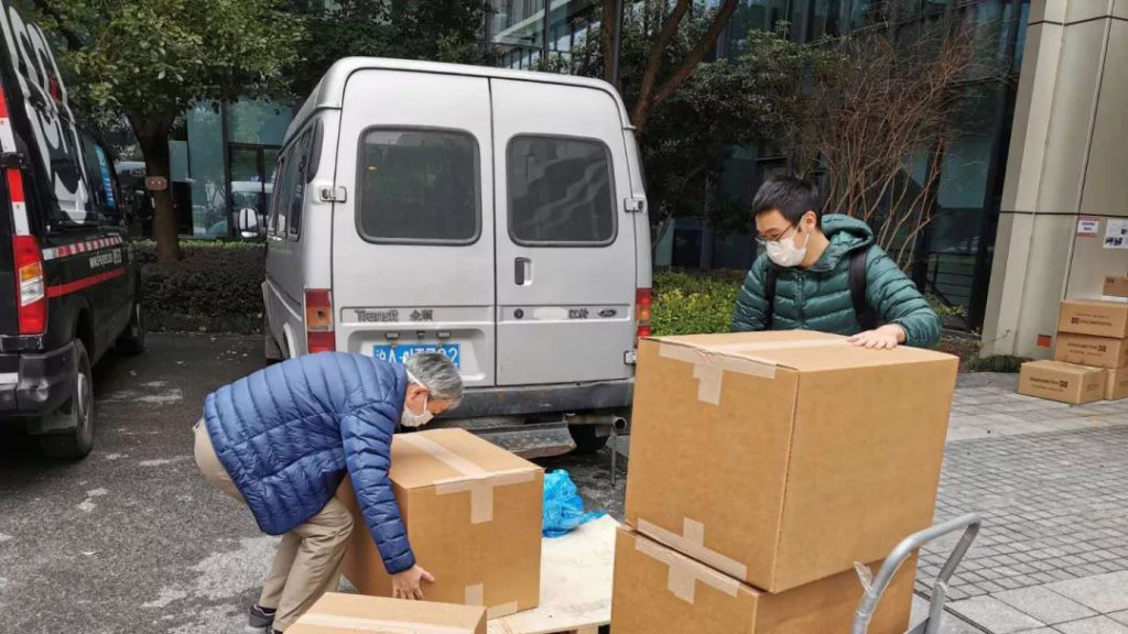 两名戴口罩的人在车辆旁转移纸箱