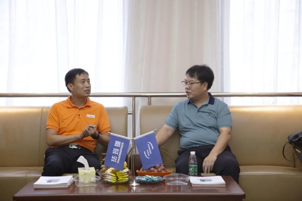 两名男子坐在沙发上互换，桌上摆有蓝色标志旗